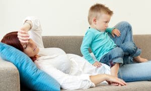 Træt og dvask mor på sofa med lille søn på skødet